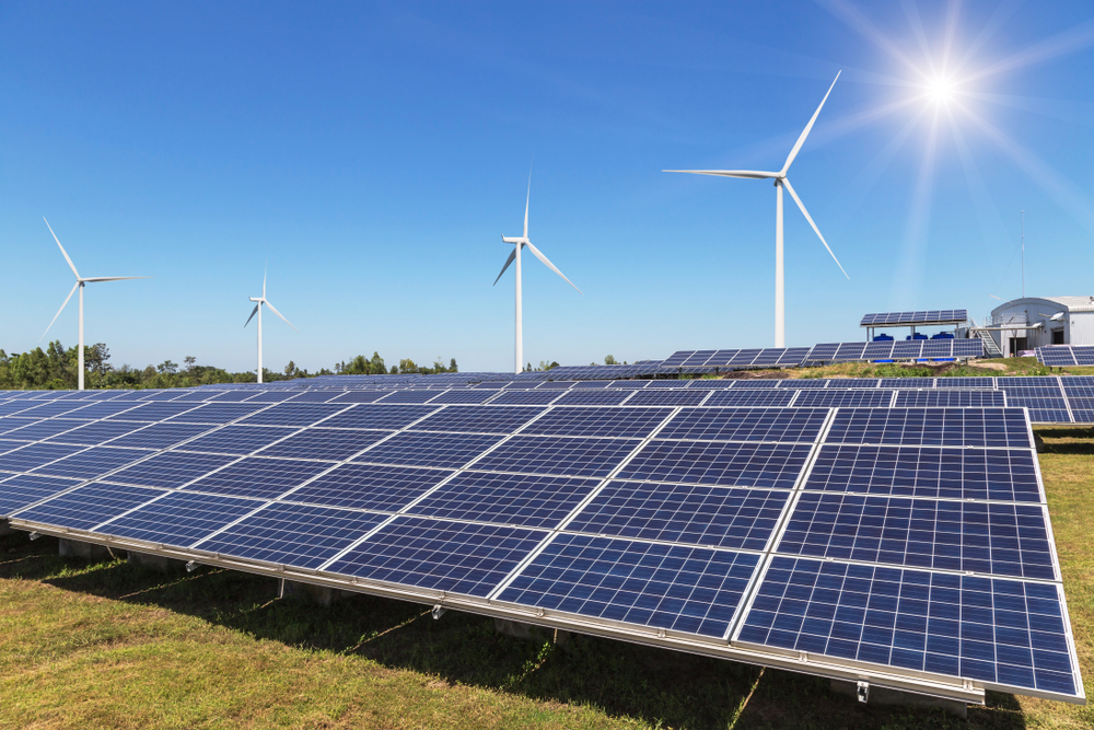 Imagem mostra painéis de energia solar com pás eólicas ao fundo