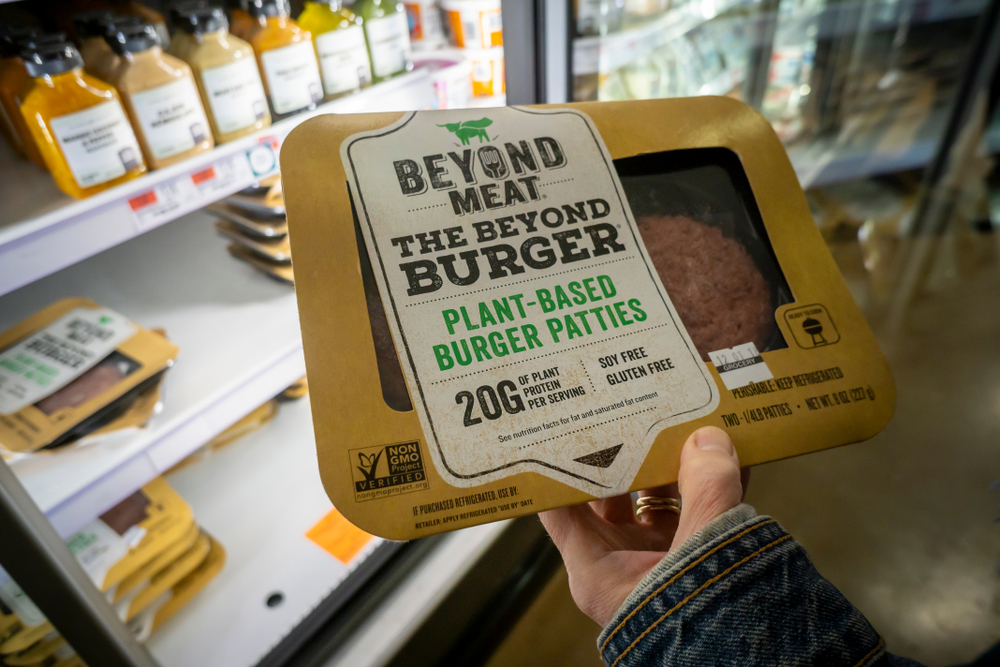 pessoa segura hambúrguer vegano da Beyond Meat no mercado em frente à geladeira.