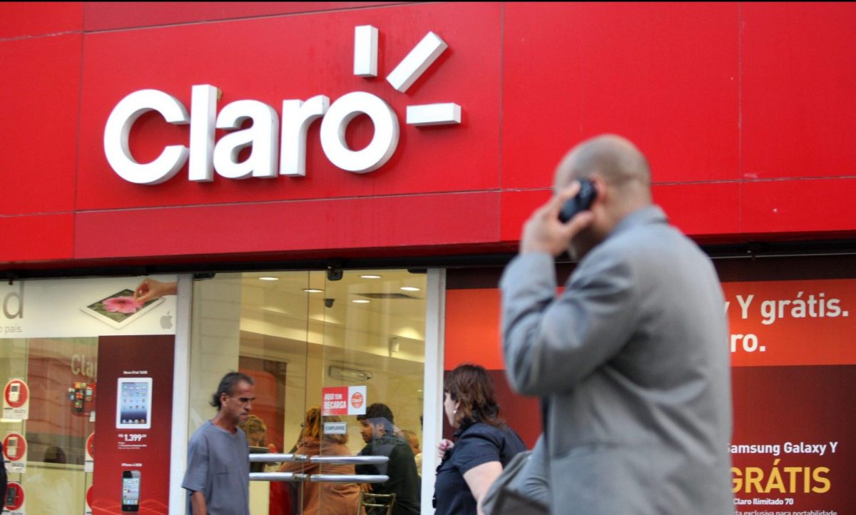 Homem usando celular caminha próximo à fachada de loja da operadora Claro, no centro do Rio de Janeiro.