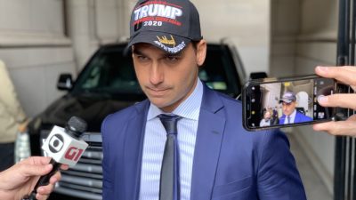 Eduardo Bolsonaro com boné escrito "Trump" no meio de repórteres.