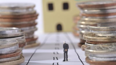 Imagem traz miniatura de idoso ao lado de pilhas de moedas