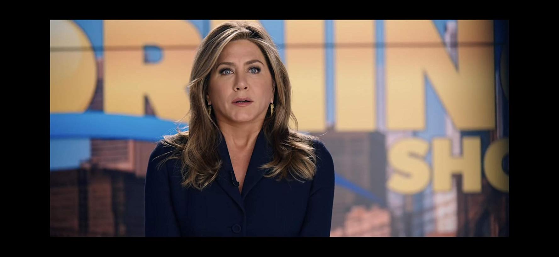 Jeniffer Aniston sentada em frente a um fundo de jornal