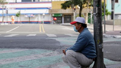 homem sentado encostado a poste com máscara em meio à pandemia do novo coronavírus