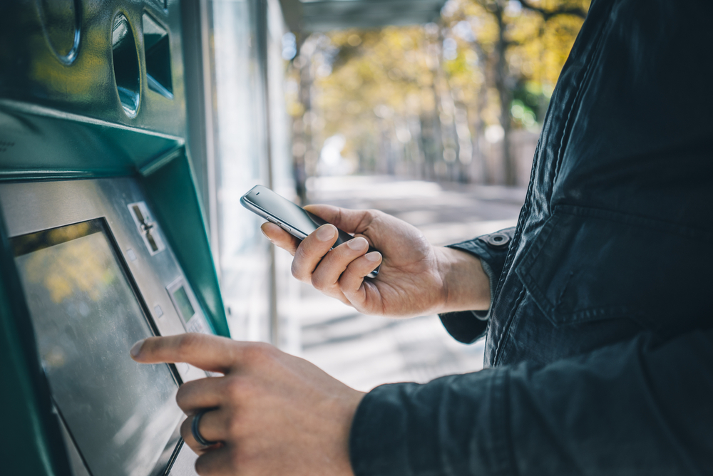 mãos masculinas usando telefone inteligente enquanto digita em ATM, caixa eletrônico de banco | Banco Central Bancos Digitais