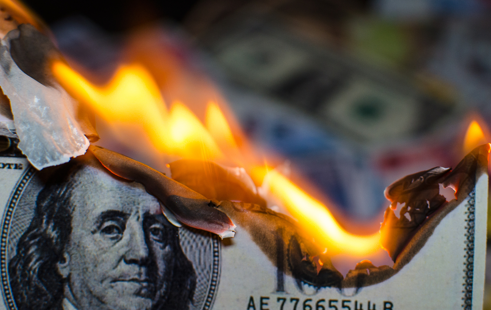 Nota de dólar queimando, simbolizando a inflação