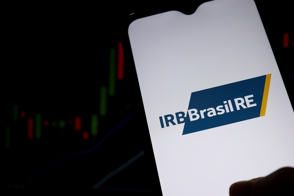 Tela de celular mostra logotipo do IRB Brasil RE com gráfico ao fundo