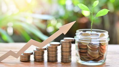 Moedas empilhadas,uma dos lado da outra, em tamanho ascendente, com montagem de seta indicando crescimento e um pote com moedas ao final (direita), simbolizando investimentos lucrativos