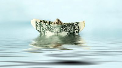 dólar em formato de barquinho de papel sobre a água