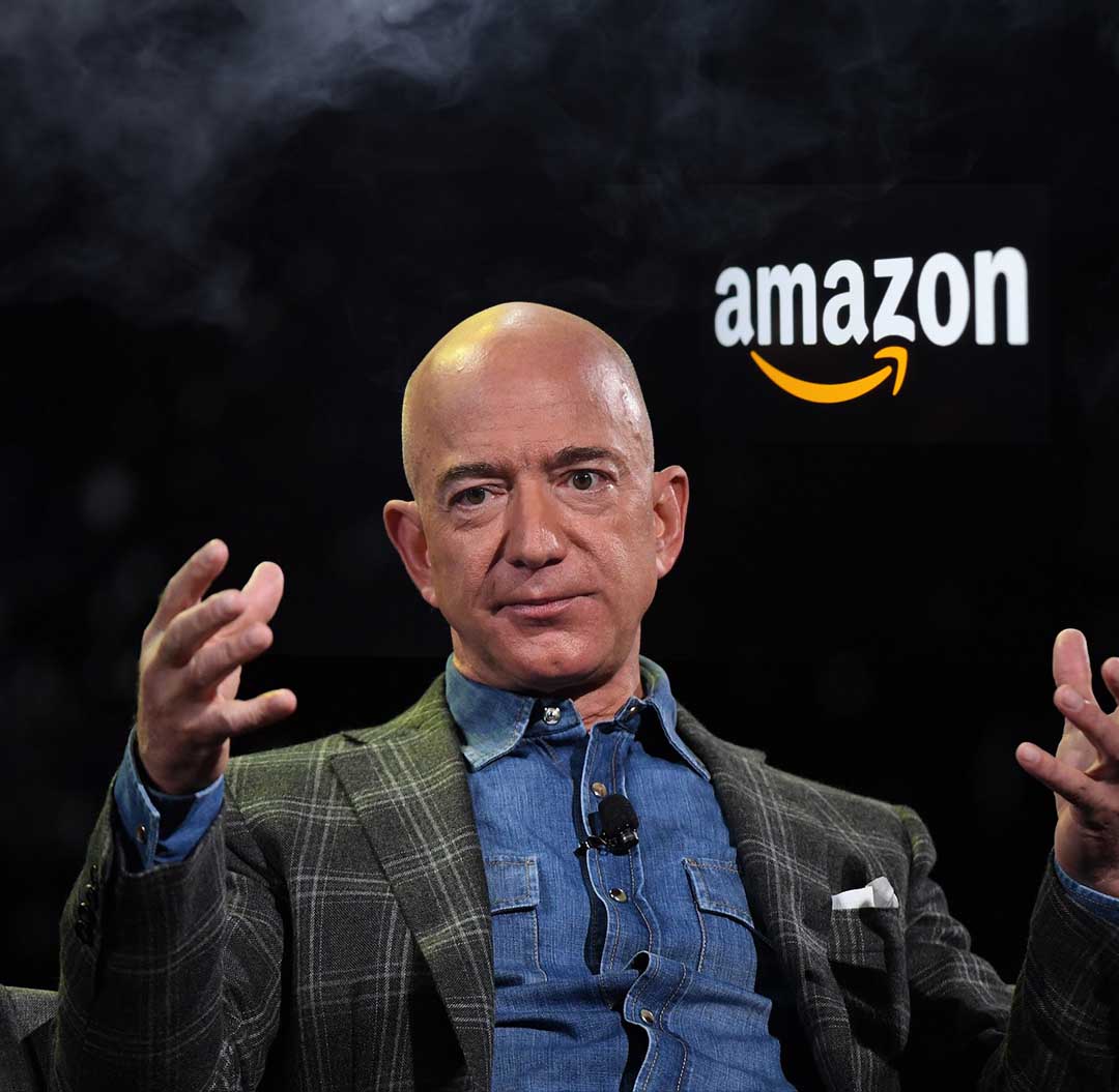 jeff bezos sentado com logo da amazon no fundo