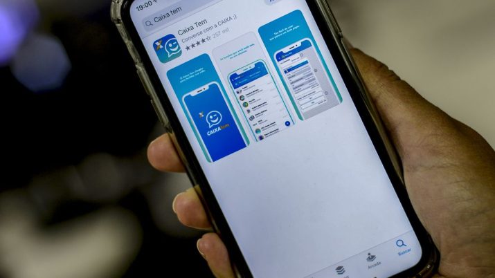 Mão segurando celular com o aplicativo Caixa Tem aberto na loja de apps