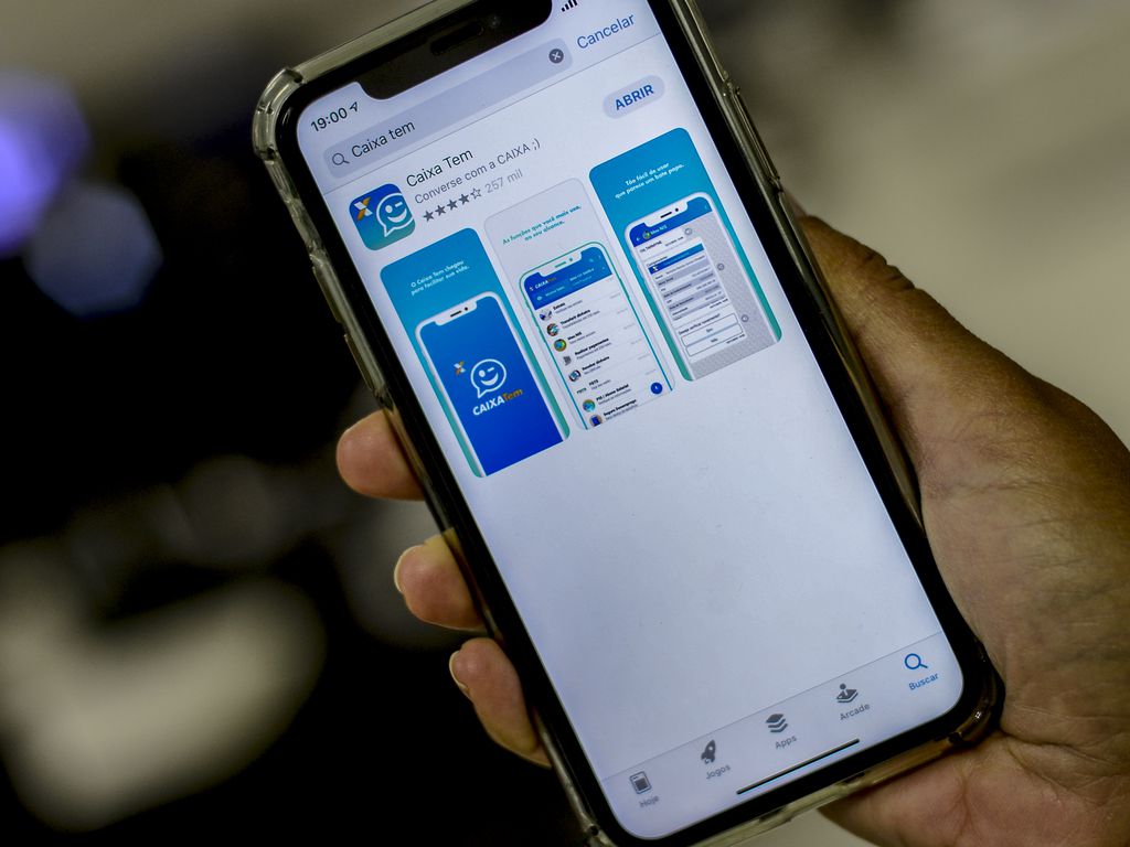 Mão segurando celular com o aplicativo Caixa Tem aberto na loja de apps