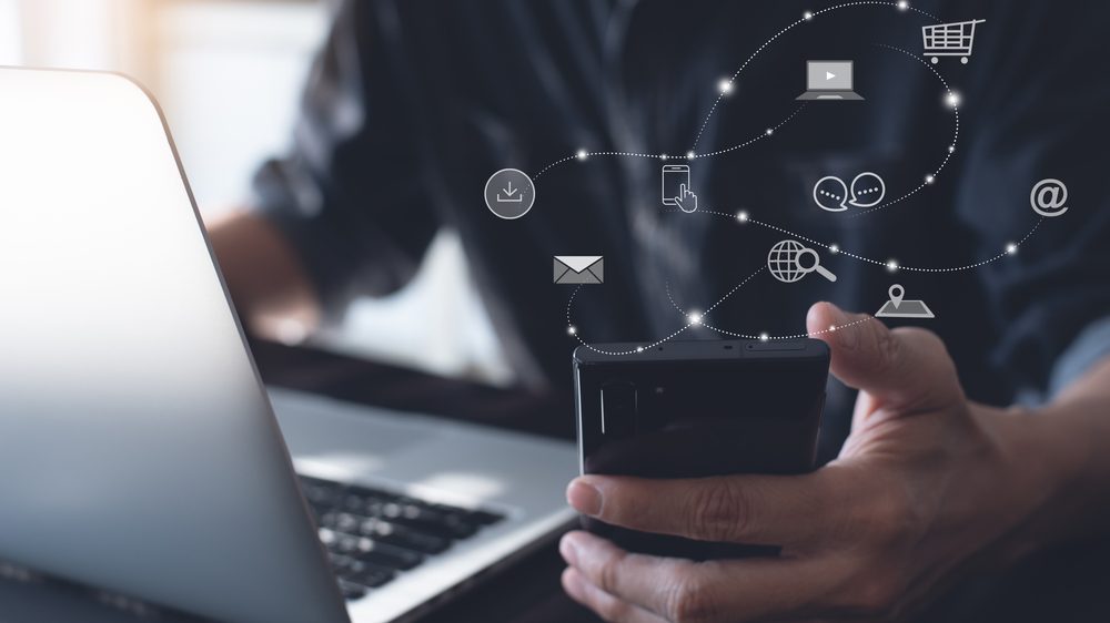 Tecnologia: Homem segurando um celular rodeado de ícones de e-mail, download, computador, pesquisa na internet, bate-papo, localização e mais