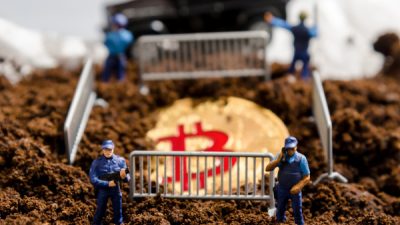 Policiais em miniatura cercam um bitcoin parcialmente enterrado | Coinbase Criptomoedas