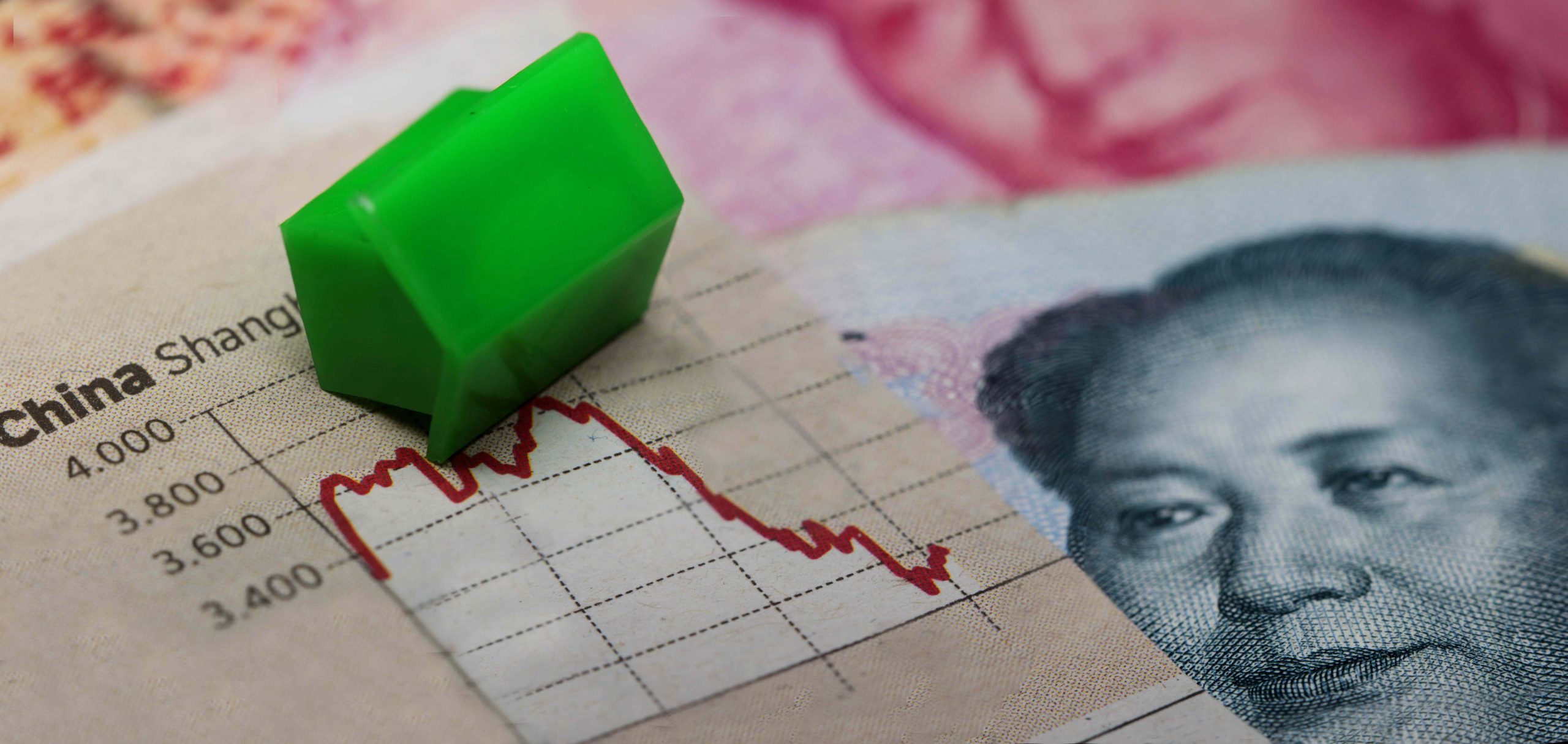 Miniatura verde em formato de casa caída sobre uma gráfico ilustrando a situação do setor imobiliário da China