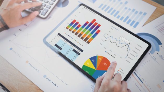 Pessoa mexe com planilhas, calculadoras e tablet, administrando seu dinheiro e investimentos