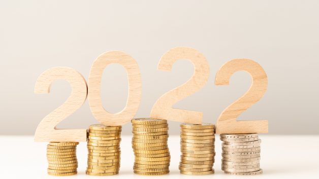 Números de madeira formando "2022" sobre pilhas de moedas