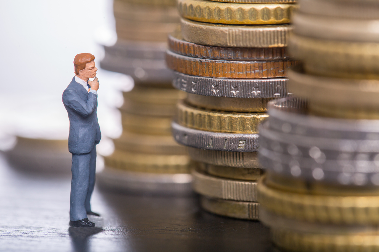 Miniatura de um homem encarando pilhas de moedas | bolsa dividendos