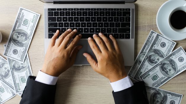 Imagem mostra laptop ao lado de notas de dinheiro