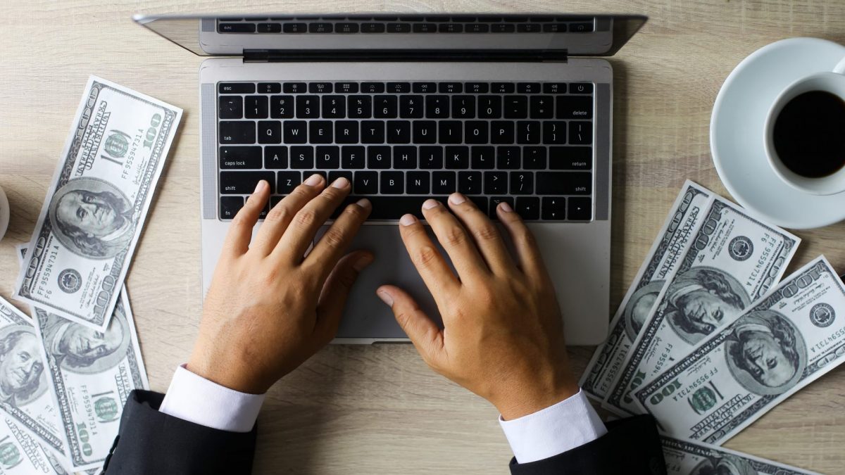 Imagem mostra laptop ao lado de notas de dinheiro