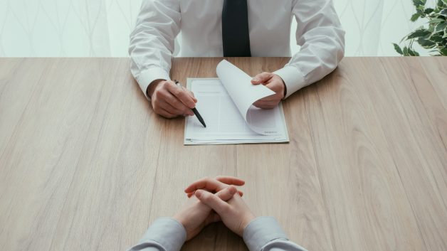 Examinador lendo um currículo durante uma entrevista de emprego; vagas abertas