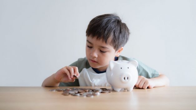 Menino colocando moedas em cofrinho de porquinho