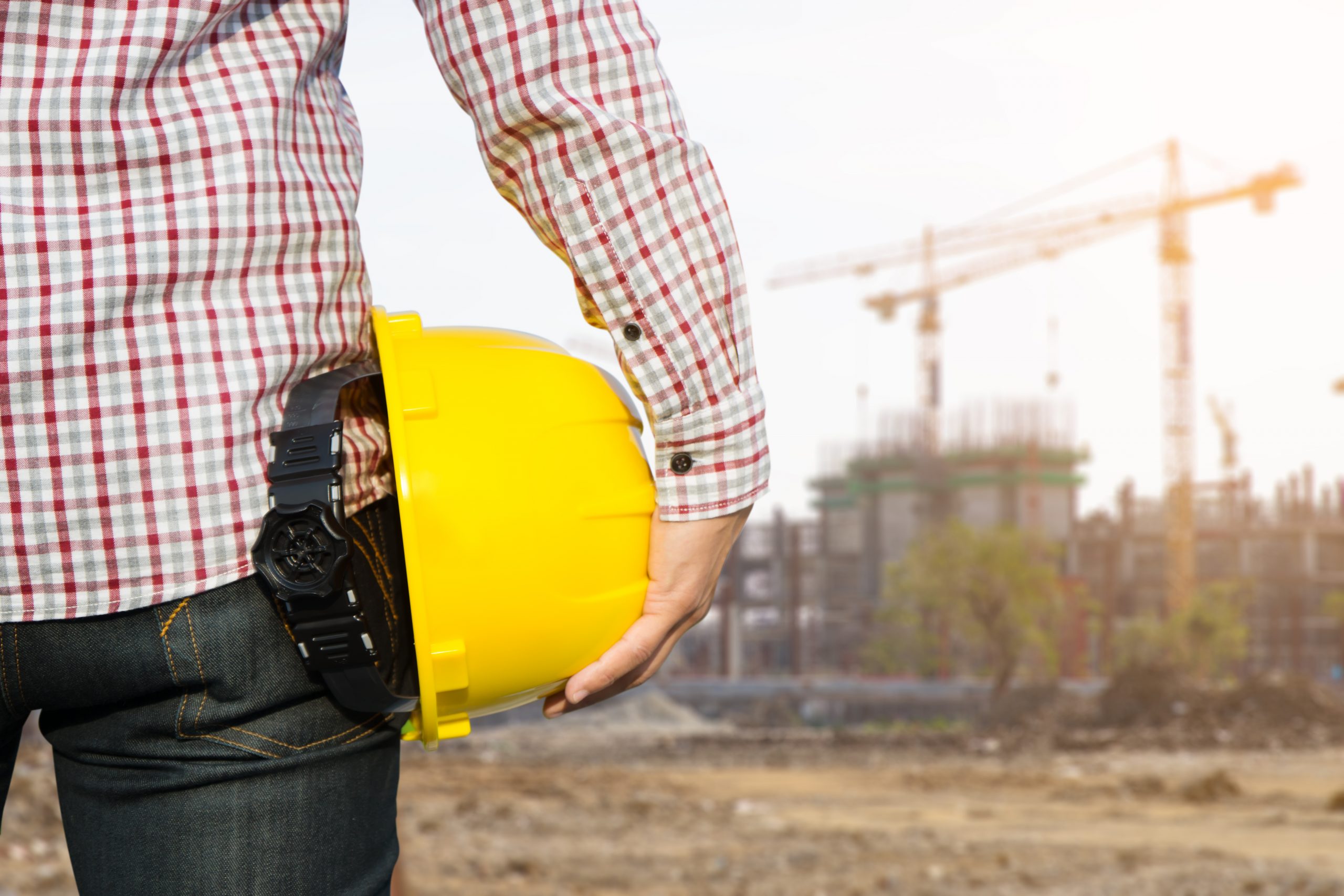 Engenheiro parado em frente a um canteiro de obras segura um capacete de segurança amarelo | Incorporadoras, ações
