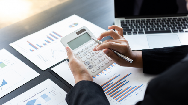 pessoa usando calculadora e planilhas com gráficos sobre a mesa; Simples Nacional