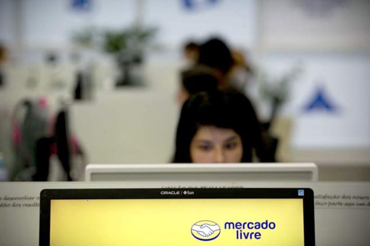 vagas; mulher mexendo no computador ao fundo; no primeiro plano, imagem do logo do Mercado Livre em tela de computador