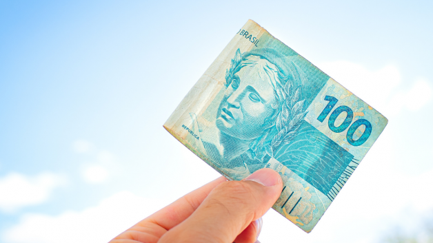 Mão segura nota de 100 reais. representando "bônus" do Governo. Dívidas
