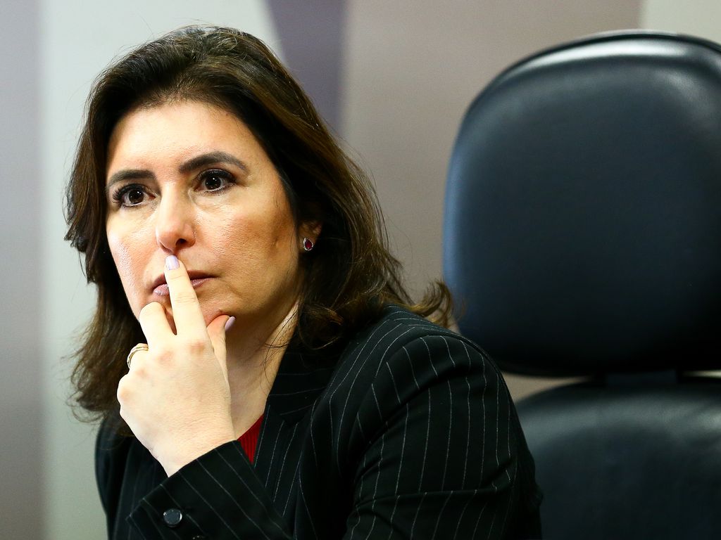 Senadora Simone Tebet, pensativa, com os braços apoiados na mesa e uma das mãos na boca