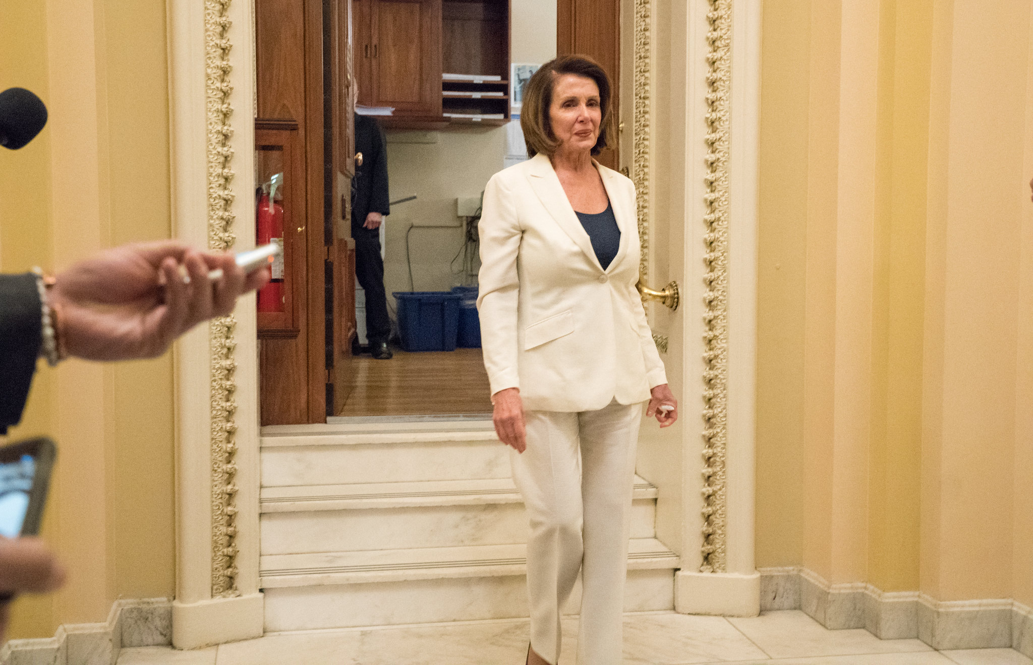Nancy Pelosi, a presidente da Câmara dos EUA, desce escadas com um terno branco e blusa azul