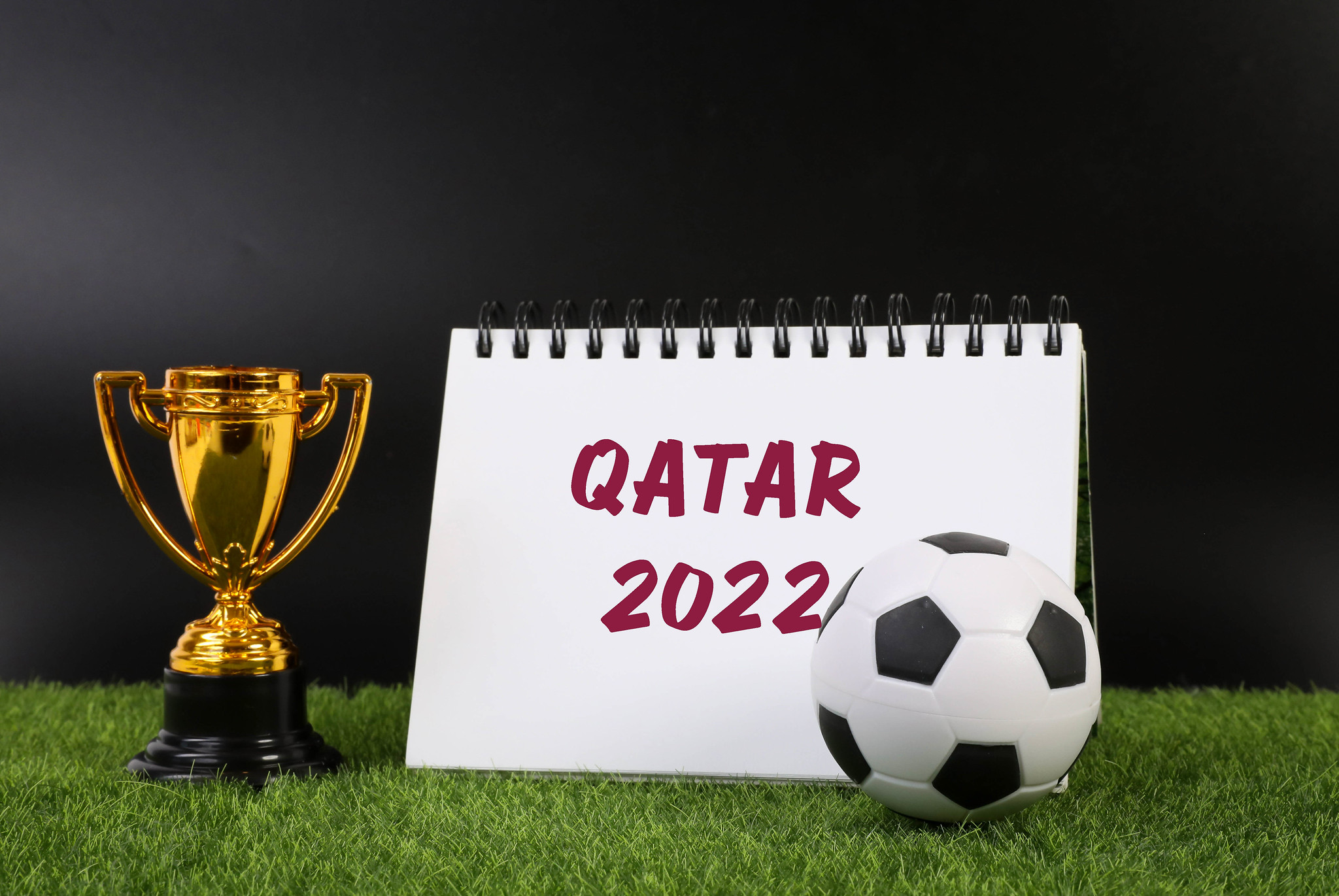Taça dourada, calendário escrito Catar 2022 e uma bola de futebol sobre o gramado; jogos do Brasil Copa 2022