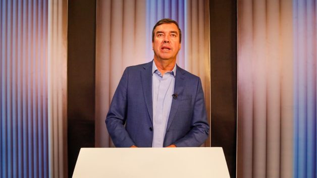 Homem em frente a um púlpito vestindo terno azul escuro e camisa azul clara