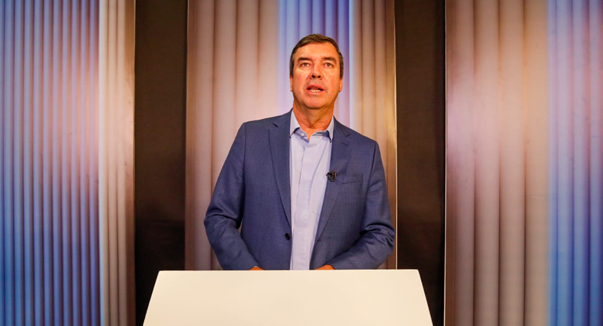 Homem em frente a um púlpito vestindo terno azul escuro e camisa azul clara