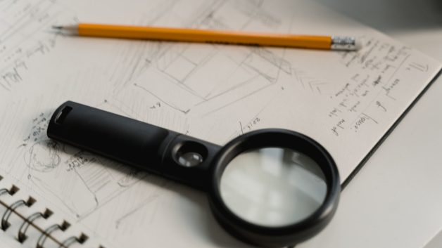 Lupa preta e lápis sobre um caderno com contas em uma página branca