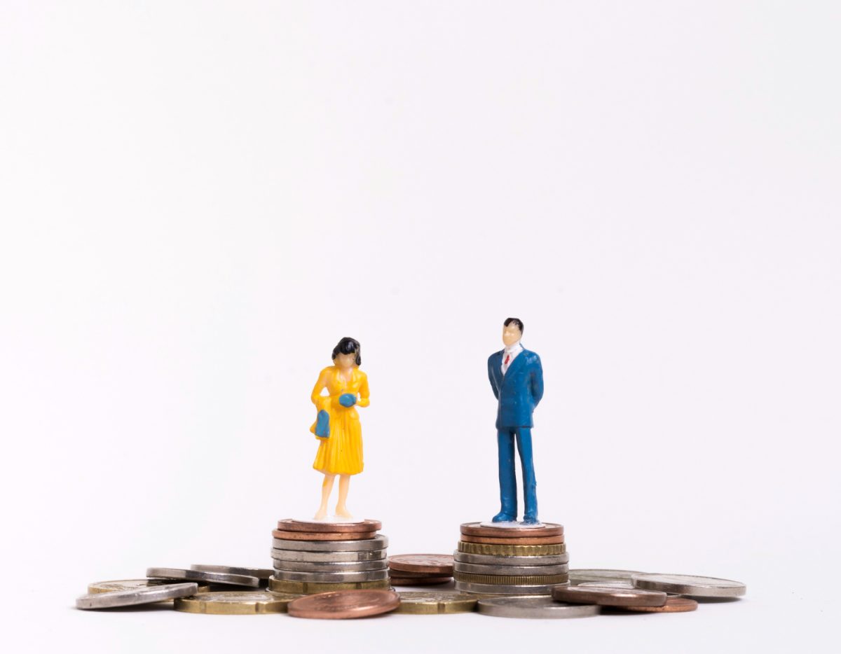 homem com terno azul e mulher de vestido amarelo, ambos em pé, cada um sobre uma torre de moedas representando a igualdade salarial