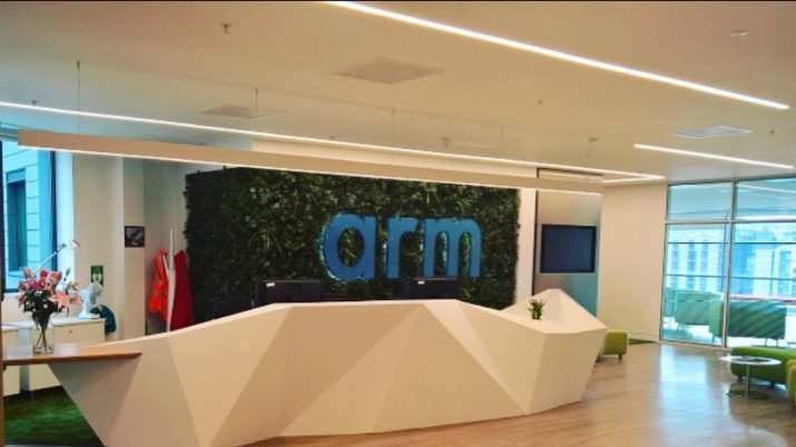 Entrada da empresa Arm, nos EUA. Logo em azul, com parede de folhas e um balcão branco.