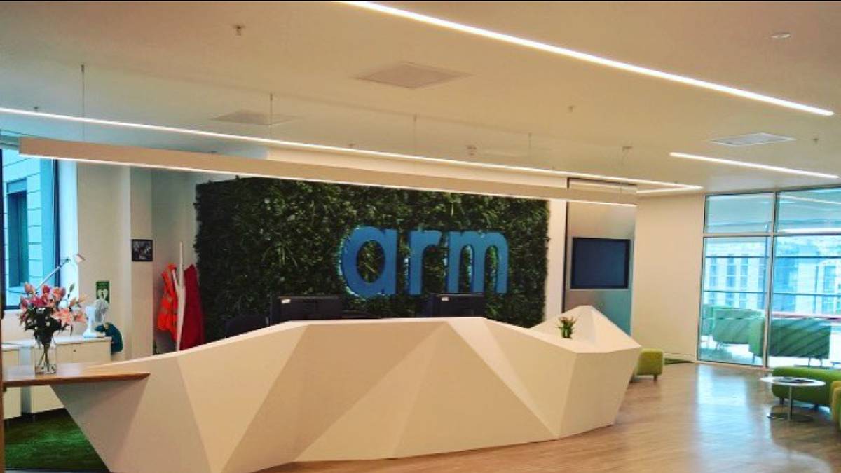 Entrada da empresa Arm, nos EUA. Logo em azul, com parede de folhas e um balcão branco.
