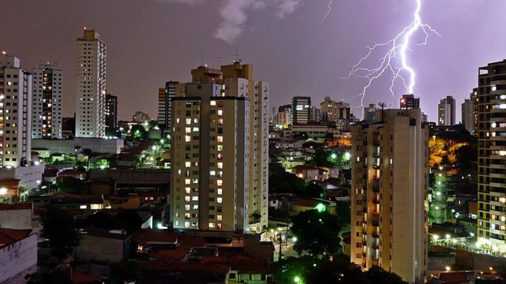 Foto de uma cidade com prédios, a noite, com raios caindo do céu