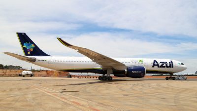 Avião da companhia de aviação Azul estacionado, com céu azul ao fundo e terrenos em volta.