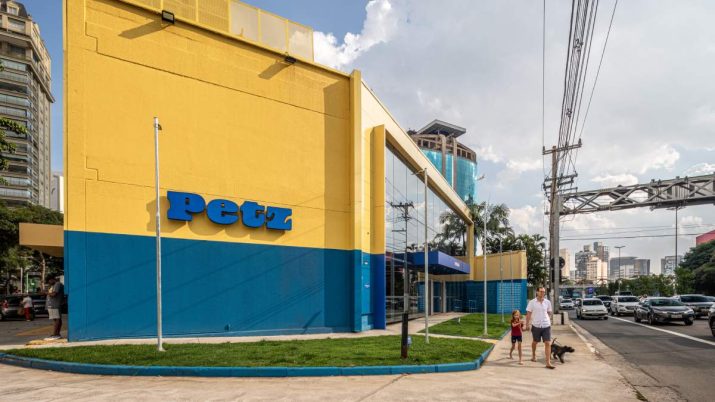 Loja Petz vista da lateral, com nome da empresa na frente, canteiro com grama e um homem passeando com um cachorro e uma criança