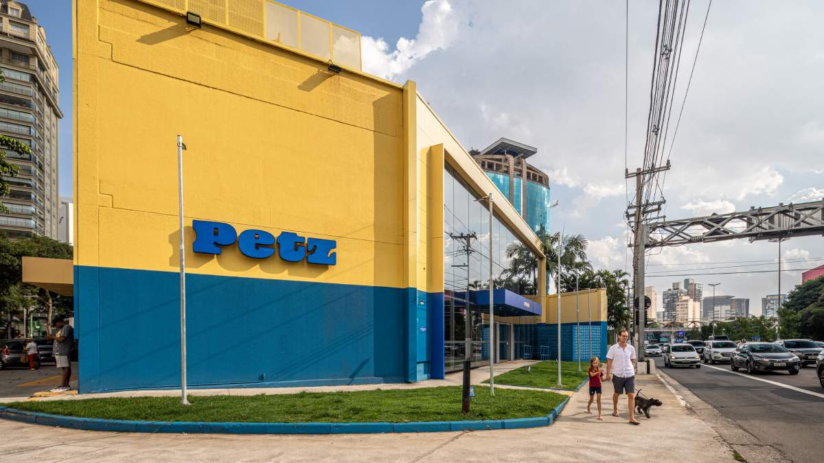 Loja Petz vista da lateral, com nome da empresa na frente, canteiro com grama e um homem passeando com um cachorro e uma criança