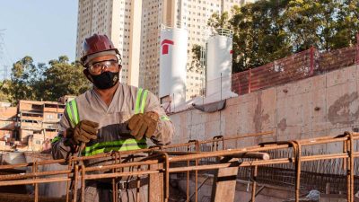 Técnico de construção no primeiro plano. Atrás, duas torres com símbolo vermelho da Tenda e prédios.
