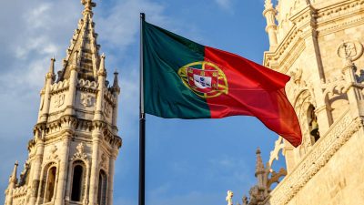 Imagem de uma bandeira de Portugal com o Mosteiro dos Jerónimos ao fundo