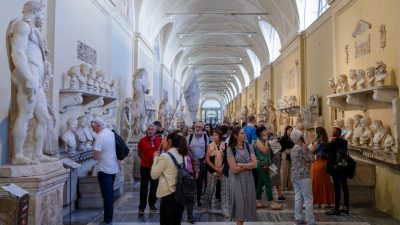 Turistas olhando para esculturas antigas de romanos no corredor do Museu Chiaramonti na Cidade do Vaticano
