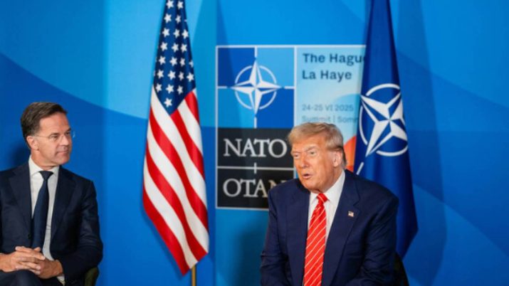 Imagem mostra Donald Trump vestindo terno azul e gravata vermelha. Ele está sentando em uma cadeira ao lado do presidente da Otan, Mark Rutte, que também usa terno escuro e camisa branca. De fundo, a bandeira dos EUA e o símbolo da Otan.