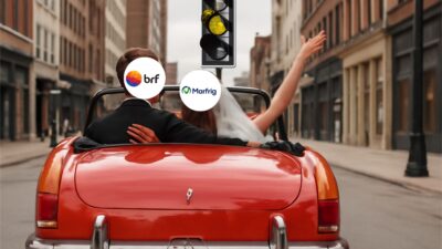 Imagem de um casal em um carro vermelho de casamento com os logotipos da BRF e Marfrig no lugar de seus rostos, passando por um semáforo amarelo em uma rua da cidade.
