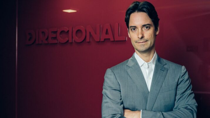 A imagem mostra o CEO da Direcional, Ricardo Gontijo, de terno cinza, posando em frente a uma parede com o logotipo da Direcional visível ao fundo. Ele está com os braços cruzados e tem uma expressão séria e confiante