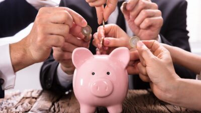 Investidores colocando moedas em cofre de porquinho.