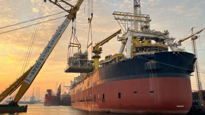 Navio-plataforma de petróleo em construção em um estaleiro, com guindastes realizando a instalação de módulos sobre a embarcação ao pôr do sol